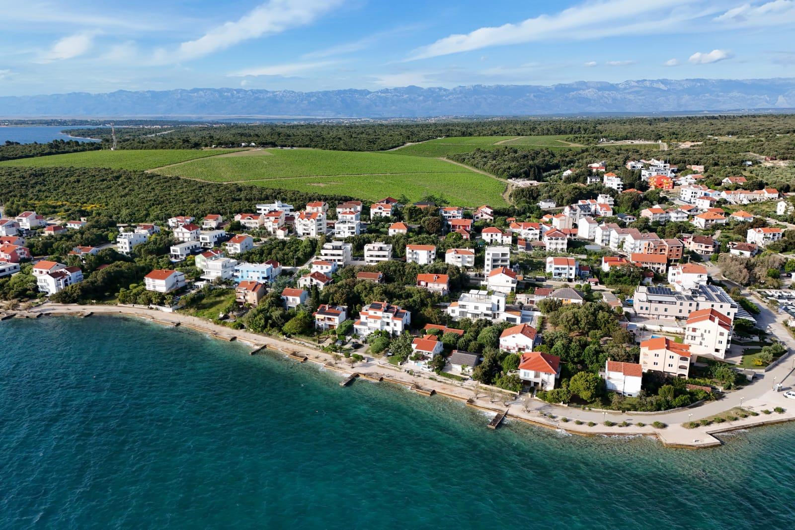Obala Petrčana iz zraka — šljunčana plaža, kuće uz more i vinogradi u zaleđu